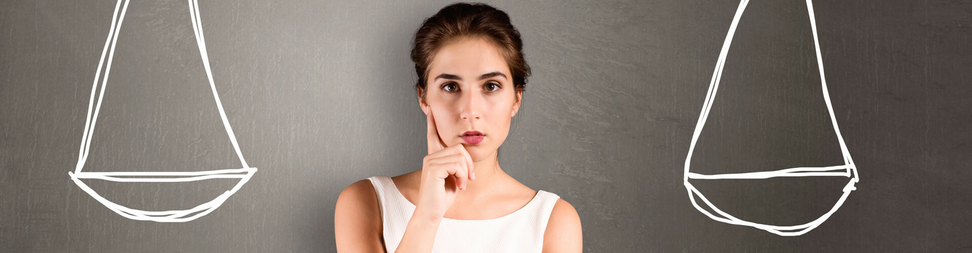 Junge Frau steht nachdenklich zwischen zwei Waagschalen, die an eine Tafel hinter ihr gemalt sind