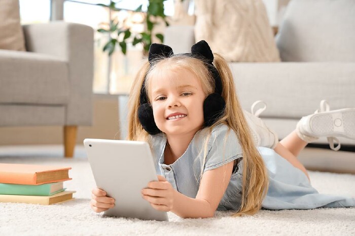 kleines Mädchen liegt im Wohnzimmer am Boden und hält iPad in den Händen