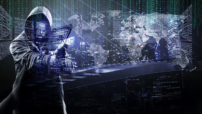 © Thaut-Images/stock.adobe.com Symbolbild für Internetkriminalität, auf schwarzem Hintergrund sieht man die Stilette eines Mannes mit Kapuzenjacke, der einen Bildschirm trägt