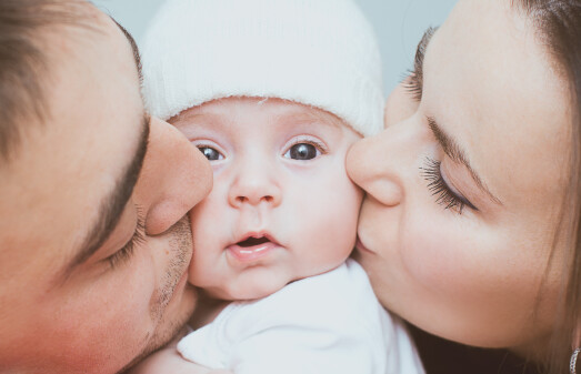 Mama und Papa küssen das Baby