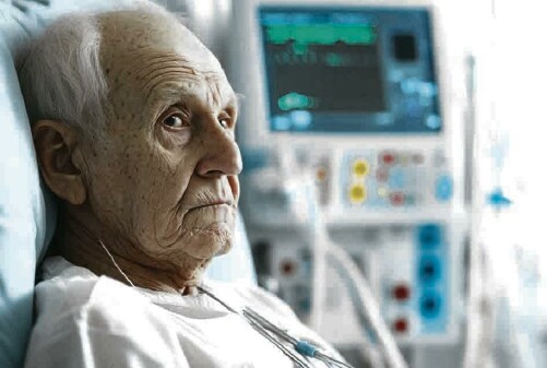 alter Mann liegt mit wei&szlig;em Nachthemd in einem Krankenbett, hinter ihm flimmert der Bildschirm eines medizinischen Ger&auml;ts