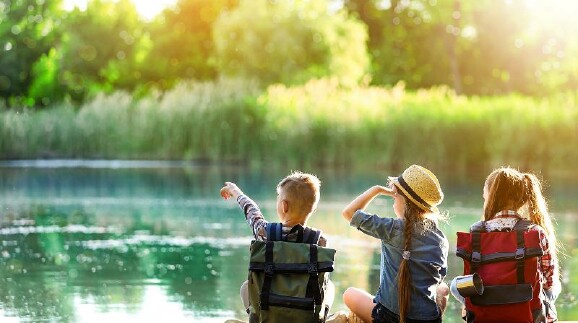 Ein Bub und zwei Mädchen sitzen am Ufer eines Sees