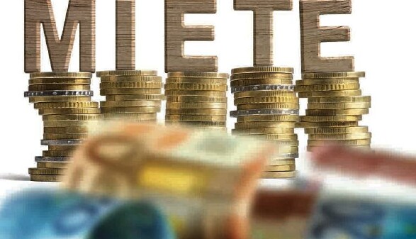 Geldscheine und aufgetürmte Münzen, darauf stehen die Holz-Buchstaben MIETE