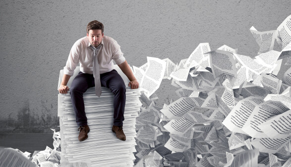 ein Mann sitzt hemds&auml;rmelig auf einem Riesenstapel Papier, im Hintergrund flattern Papiere