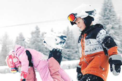 zwei Kinder mit Skihelm toben im Schnee