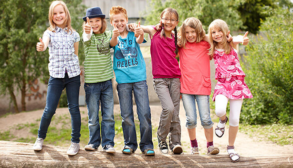 Fröhliche Kinder stehen auf einem quer liegenden Baumstamm