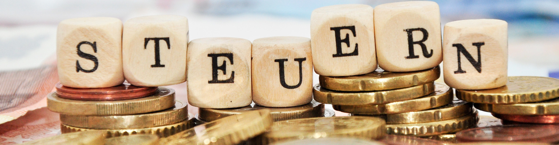 Buchstabenwürfel, welche auf einem Stapel Euro-Münzen liegen, bilden das Wort "Steuern"