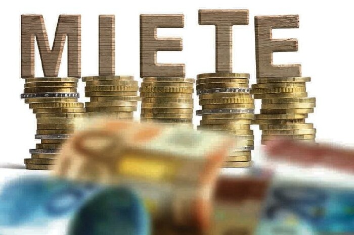 Geldscheine und aufgetürmte Münzen, darauf stehen die Holz-Buchstaben MIETE