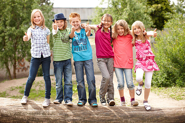 Fröhliche Kinder stehen auf einem quer liegenden Baumstamm