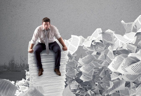 ein Mann sitzt hemds&auml;rmelig auf einem Riesenstapel Papier, im Hintergrund flattern Papiere