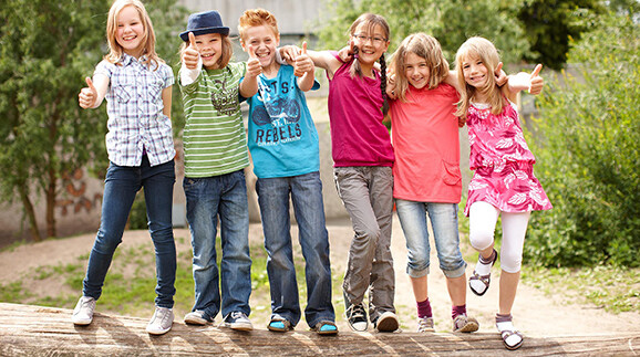 Fröhliche Kinder stehen auf einem quer liegenden Baumstamm