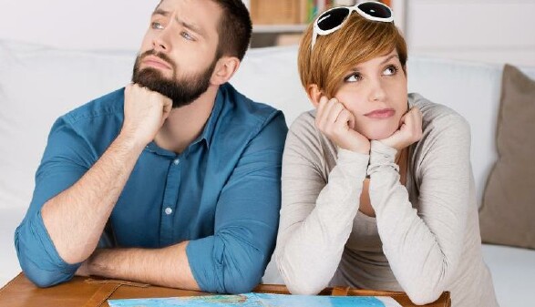 Ein Paar sitzt ver&auml;rgert mit dem Koffer und einer Landkarte in einem Zimmer