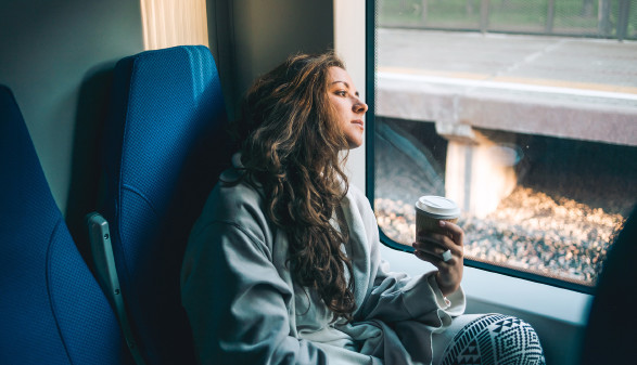 © Gregory Lee, stock.adobe.com Junge Frau mit Coffee To Go in der Hand schaut nachdenklich aus dem Zugfenster © Gregory Lee, stock.adobe.com