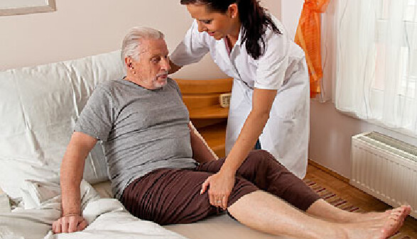 Pflegekraft hilft älterem Mann aus dem Bett