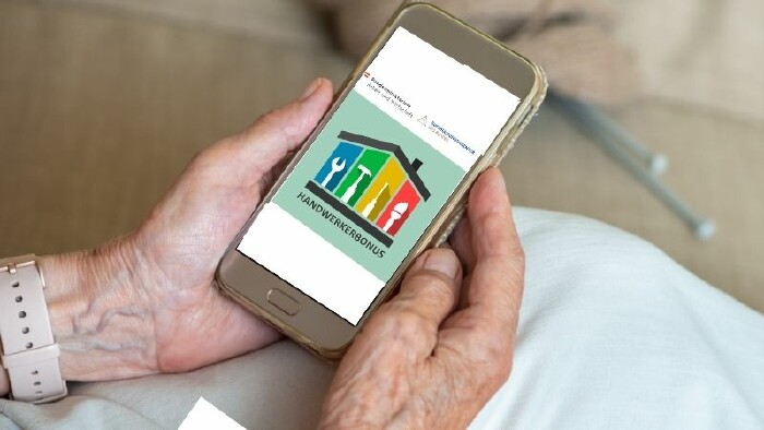 Ein Smartphone in den Händen einer älteren Person, darauf die Website zum Handwerkerbonus.