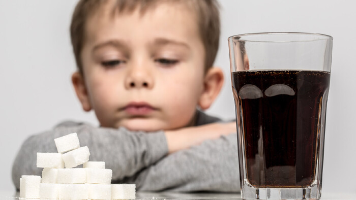 Kind sitzt vor Limonade und W&uuml;rfelzucker