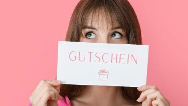 Eine Frau h&auml;lt einen Gutschein vor ihrem Gesicht.