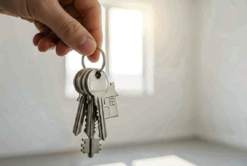 Eine linke Hand h&auml;lt einen Schl&uuml;sselbund, im Hintergrund sieht man einen leeren Raum und ein Fenster, durch das Licht einf&auml;llt.