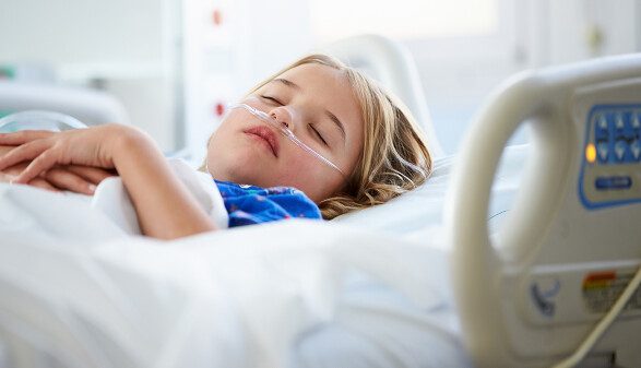 Kind liegt in einem Krankenhausbett mit einem Sauerstoffschlauch in der Nase