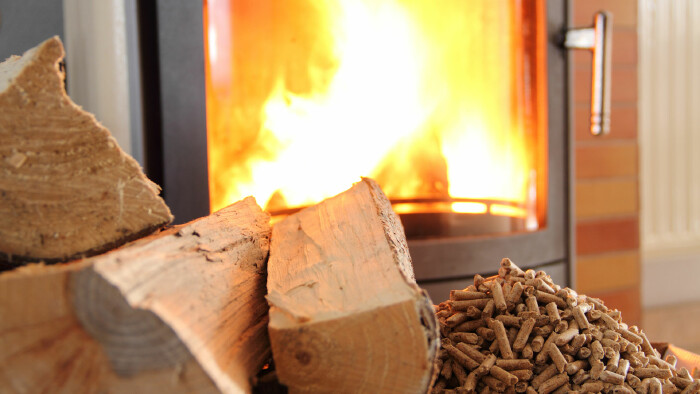 Ein brennender Kaminofen mit sichtbarer Flamme. Davor liegen Holzscheite und Holzpellets.
