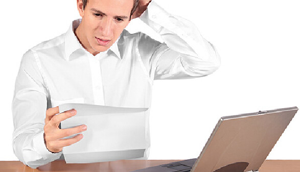 Junger Mann sitzt vor Laptop und hält einein Brief in der Hand