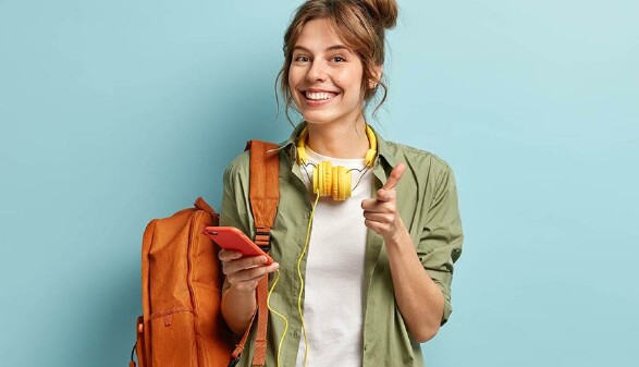 Schülerin hält Handy in der Hand und hat einen Rucksack über die Schulter gehängt