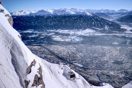 Winterliche Aussicht von der Nordkette in die Stadt Innsbruck, in der Mitte eine Godel, die gerade auf den Berg fährt