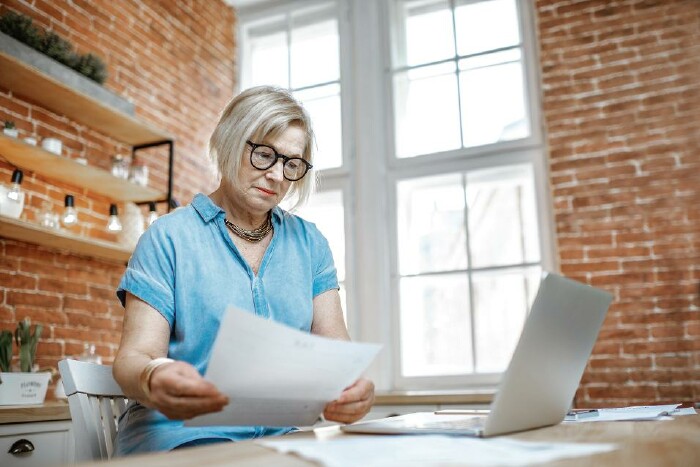 © rh2010/stock.adobe.com Frau sitzt mit Unterlagen und Laptop am Küchentisch