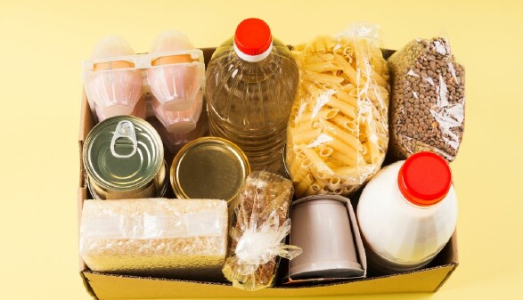 Ein Karton mit Grundnahrungsmitteln steht auf gelbem Hintergrund. © Canva