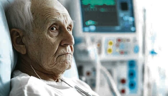 alter Mann liegt mit wei&szlig;em Nachthemd in einem Krankenbett, hinter ihm flimmert der Bildschirm eines medizinischen Ger&auml;ts