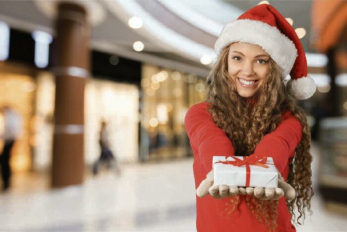 Frau mit Weihnachtsmütze steht in einem Einkaufszentrum und hält ein kleines Geschenk in ihren Händen.